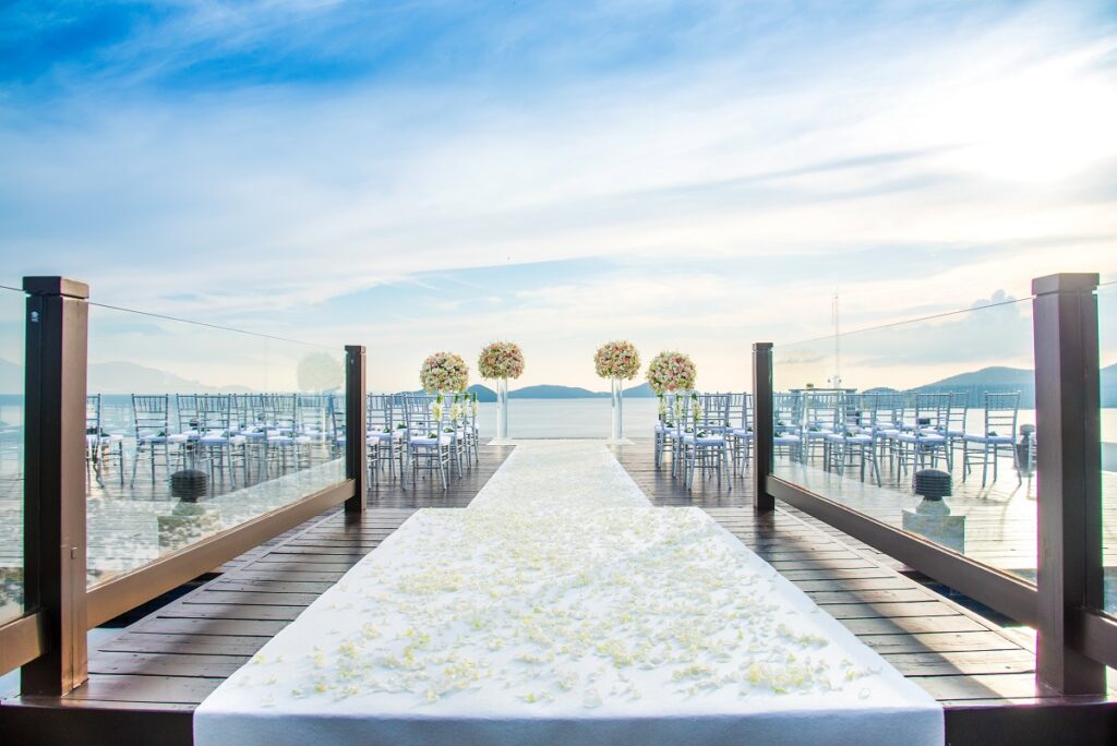 Ocean view rooftop wedding setup at a resort with a petal-covered aisle, floral arches, and elegant chairs.