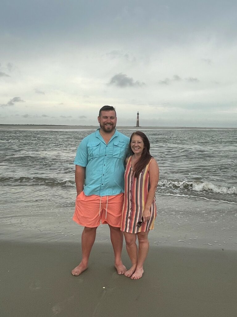 Tommie and Tori standing on the beack with sea and lighthouse in background