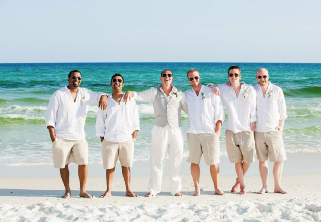 Groom and groomsmen at the beach in beach casual attire for a destination wedding, with white shirts, and khaki shorts.